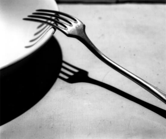 アンドレ・ケルテスによる白黒写真で、皿とフォークとテーブルに落ちる影が写されている
